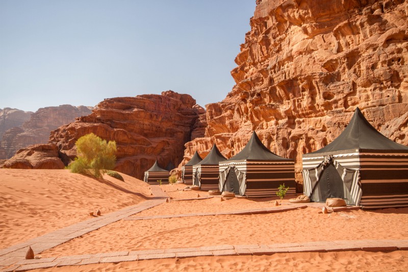 Green and white Bedouin tents sit next to tall cliffs in the desert of Wadi Rum Jordan