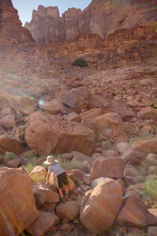 A young boy wearing a hat climbs over the red rocks of the Wadi Rum desert towards a spring discovered by Lawrence of Arabia